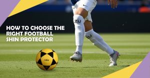 Soccer player in white kit with honey-comb patterned shin guards and a yellow football on a grass pitch.